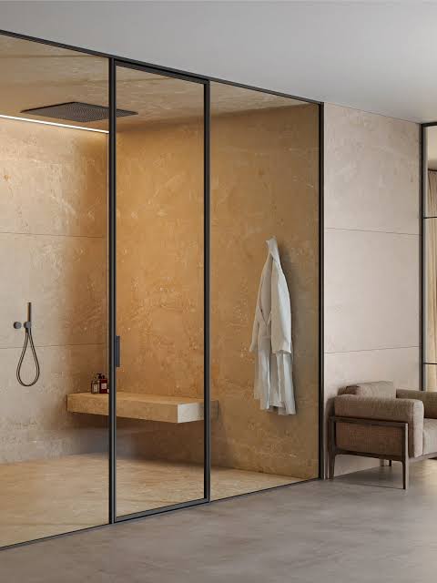 Fine dark glass profiles beside a warm stone-clad bathroom